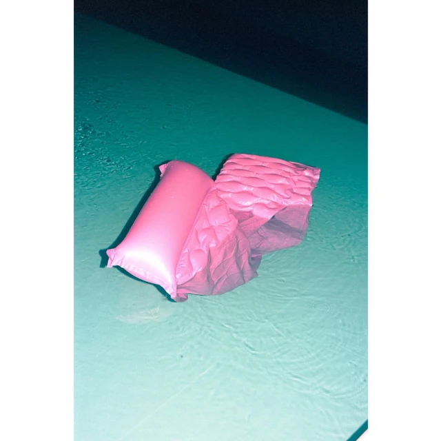 A pink inflatable float sits in a swimming pool with turquoise water and a dark shadow in the background.