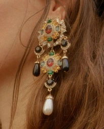 Close-up portrait of an elaborate gemstone earring with crystals, black beads, and a pearl drop on an ear.
