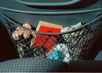 Close-up interior car shot of a mesh pocket holding a red book, pink flowers, and a snakeskin patterned item by Philippe Billemont.