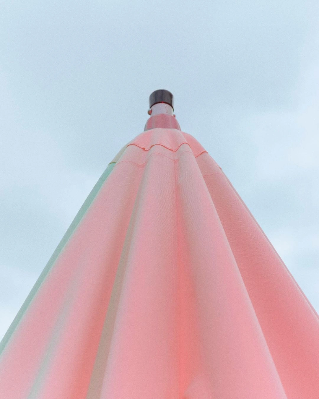Low angle shot of a large pink umbrella pointed upward against a pale grey sky in Paris by Philippe Billemont.