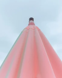 Low angle shot of a large pink umbrella pointed upward against a pale grey sky in Paris by Philippe Billemont.