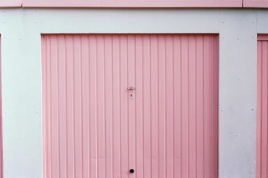 Pink corrugated metal garage door framed by white concrete walls with a small centered metal handle and lock