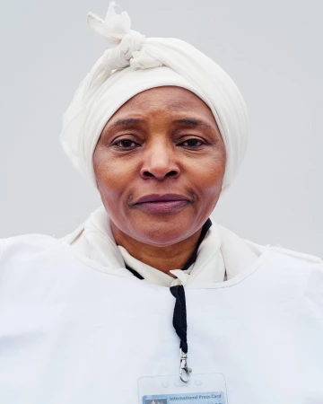 Close-up portrait of a woman with an International Press Card. She wears a white headscarf and top against a bright background.