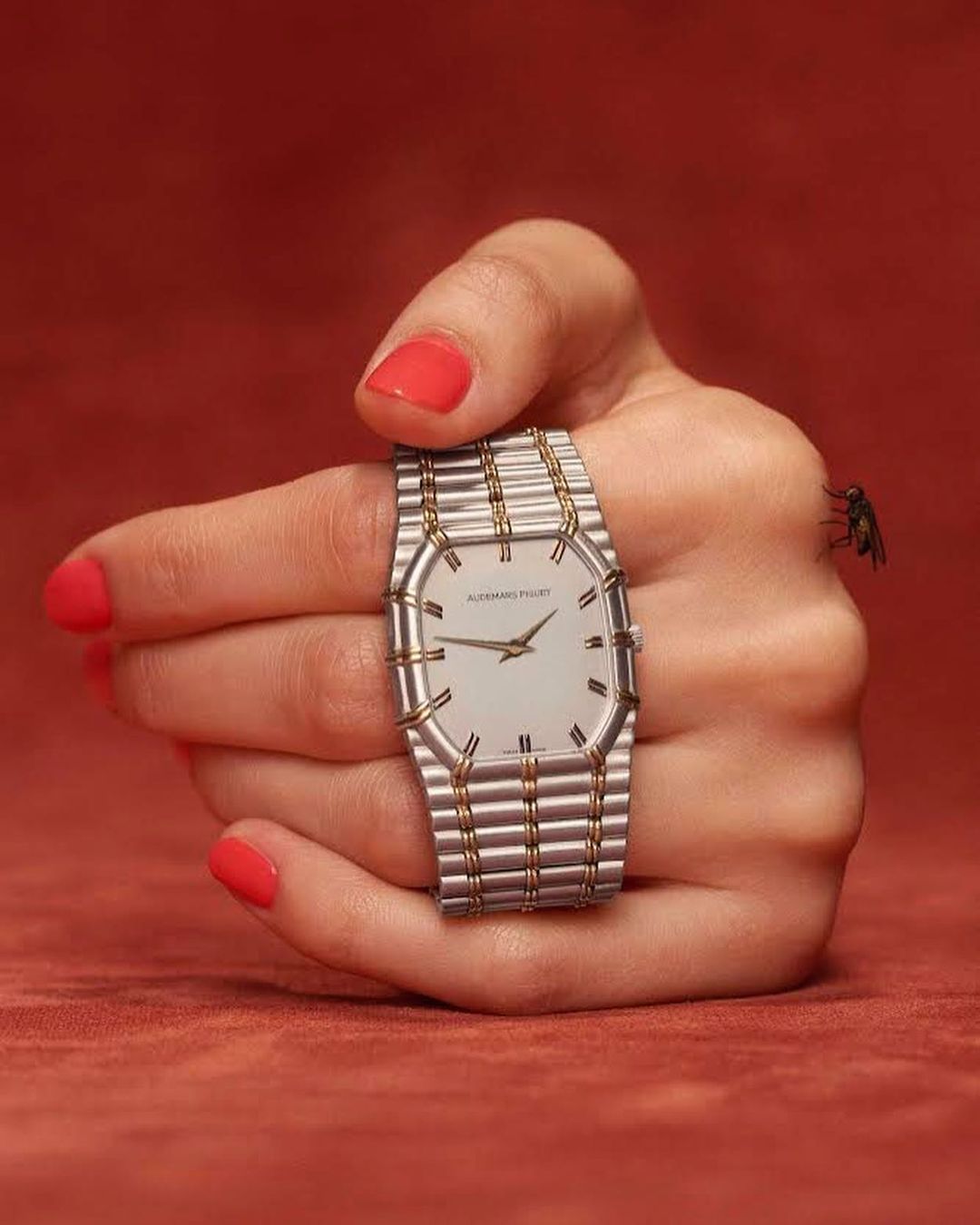 Close-up shot of an adult female hand with red nail polish, holding a luxury wristwatch with a silver and gold band, indoors.