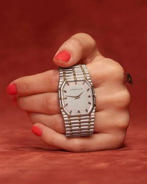 Close-up shot of an adult female hand with red nail polish, holding a luxury wristwatch with a silver and gold band, indoors.