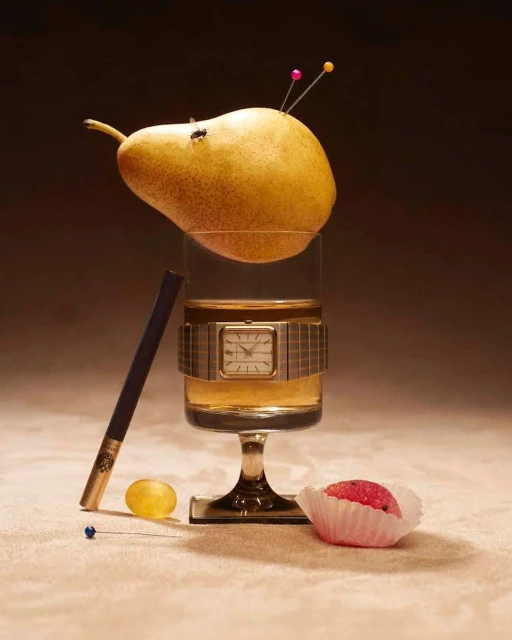 Still life of a pear resting on a stemmed glass with a watch, next to a cigarette, grape, and pin on a beige surface.