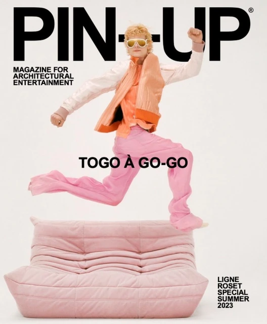 Magazine cover features a person leaping over a pink couch, wearing pink pants, and an orange jacket against a white background.