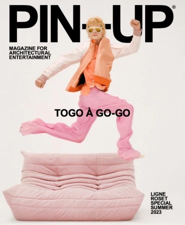 Magazine cover features a person leaping over a pink couch, wearing pink pants, and an orange jacket against a white background.