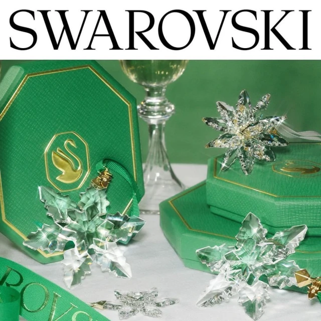 Crystal snowflake ornaments and green gift boxes arranged against a green backdrop, highlighted by a stemmed glass and Swarovski branding.