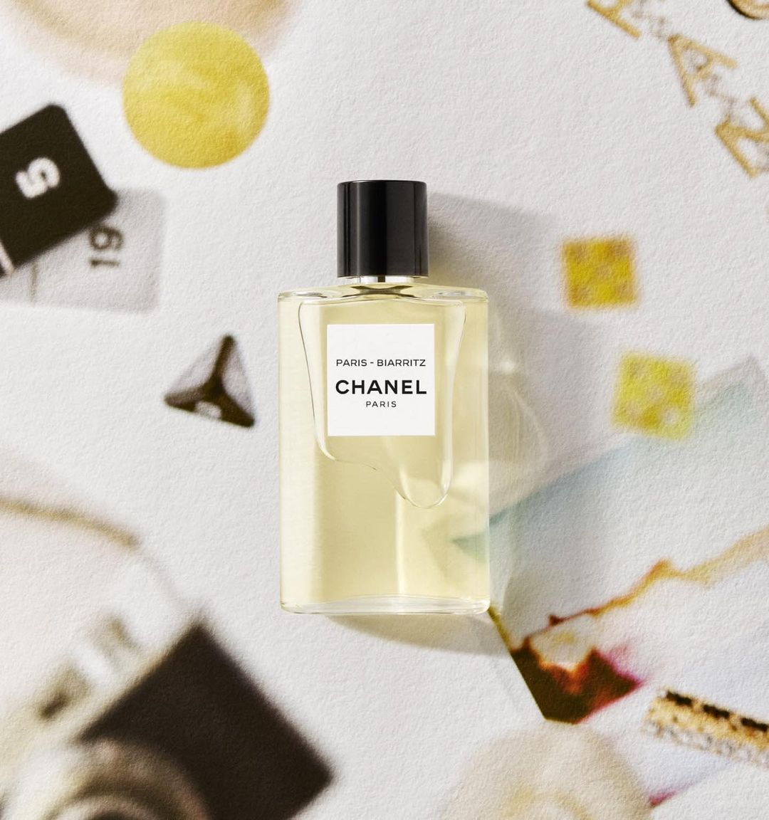 A rectangular Chanel Paris Biarritz perfume bottle resting on a textured, flat lay surface featuring assorted cards and papers.