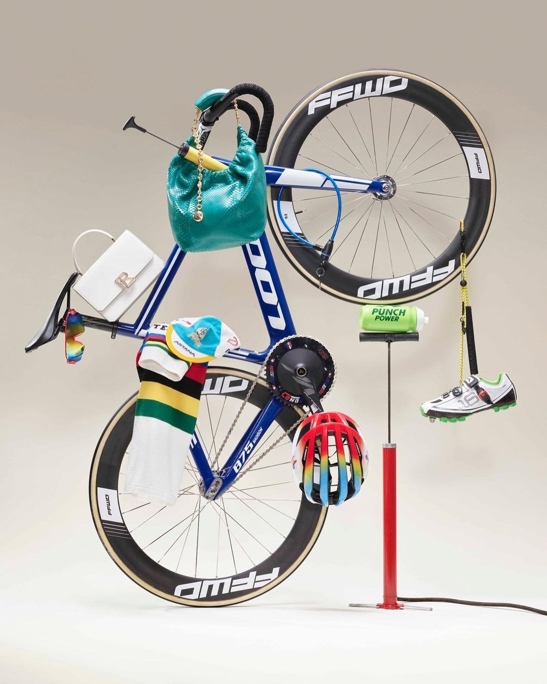 Still life studio shot of a blue and white racing bicycle with attached accessories, shoes, bags, water bottle and helmet.