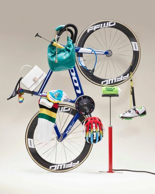 Still life studio shot of a blue and white racing bicycle with attached accessories, shoes, bags, water bottle and helmet.