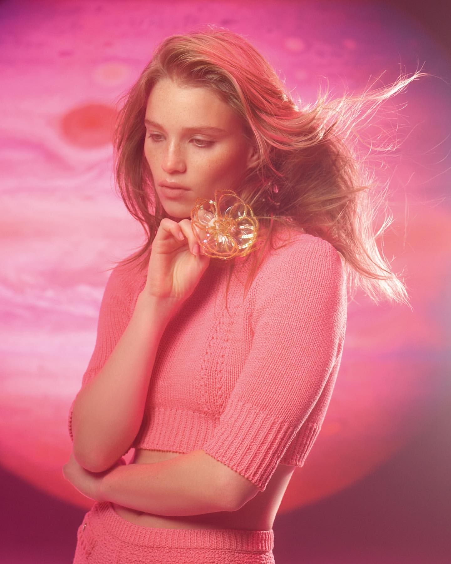 Young woman in pink knitwear holds translucent ball in a pink studio with Jupiter planet in the background, beauty shot, fashion.