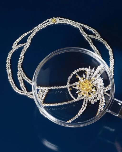 Close-up shot of an elaborate diamond necklace with a magnifying glass, set against a dark blue background, highlighting its details.
