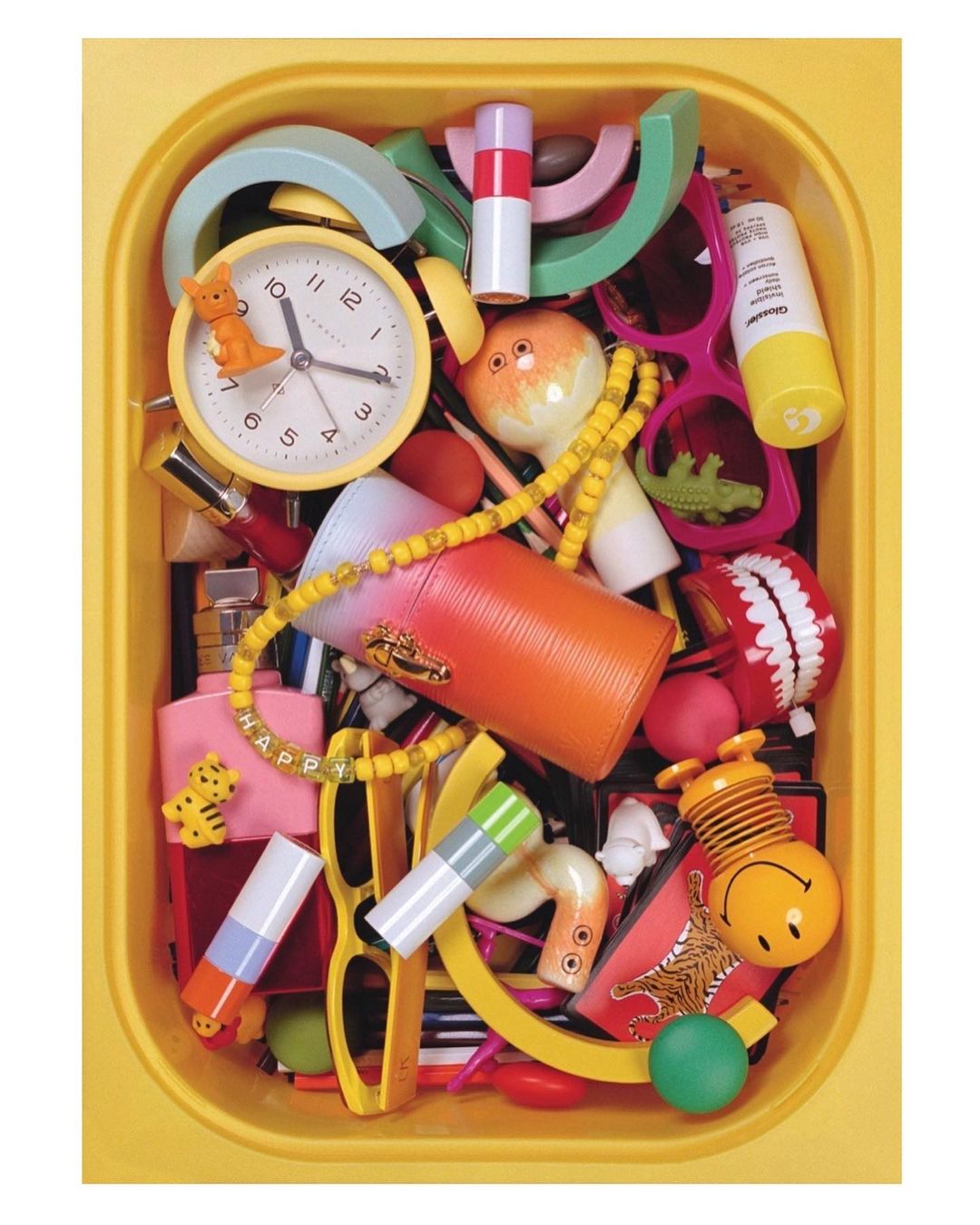 Overhead shot in a yellow container shows a collection of toys, eyewear, beauty products, beads, and household objects and novelties.