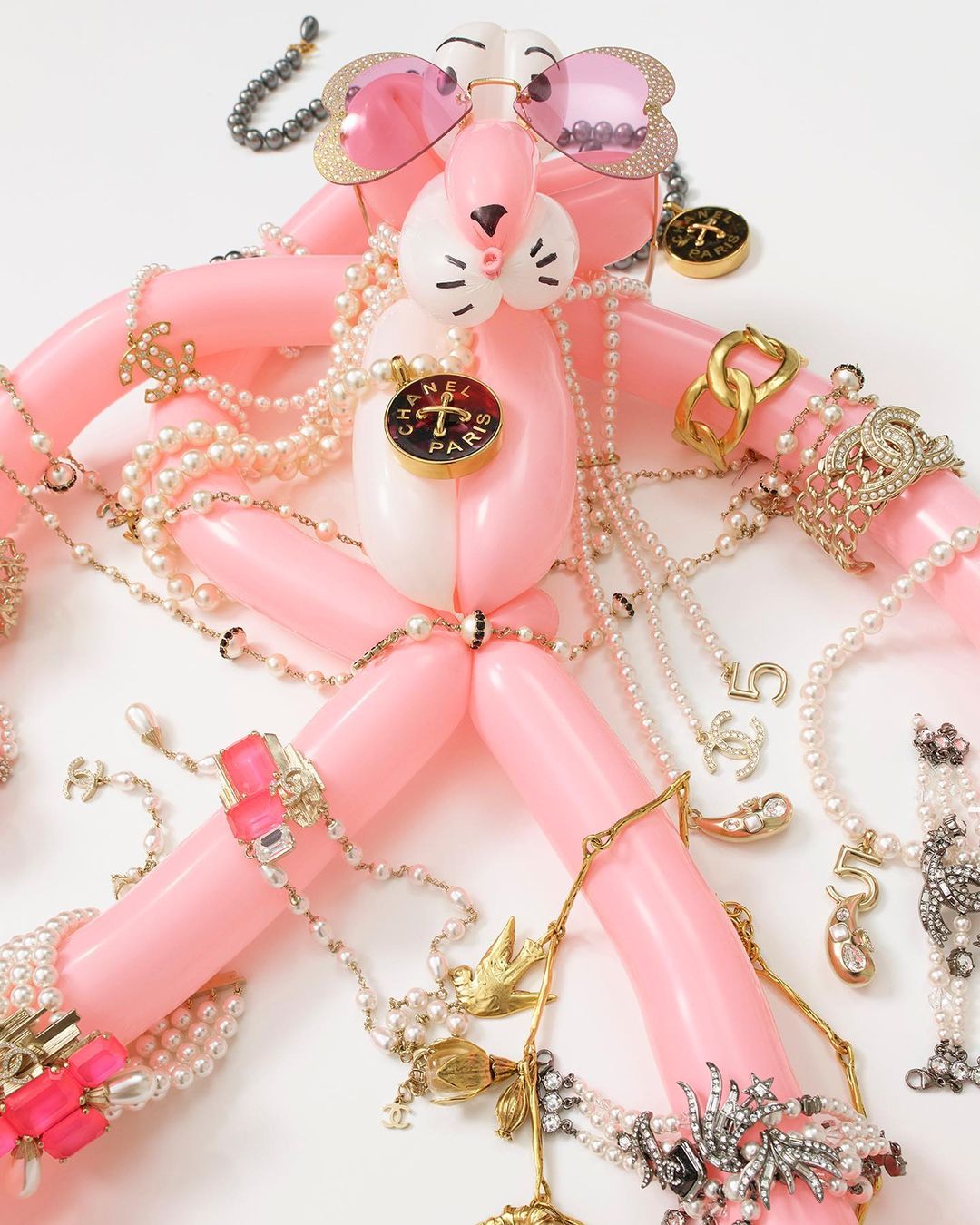 Balloon poodle sculpture with pink sunglasses, gold hoop earrings, necklaces, and a white background, showcasing whimsical fashion accessory art.