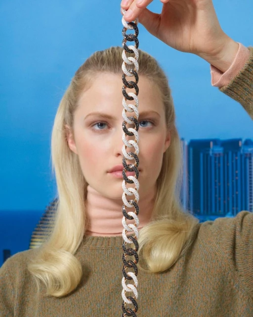 Woman presents chain-link bracelet with gem accents in a portrait against a blurred city skyline backdrop under a clear blue sky.