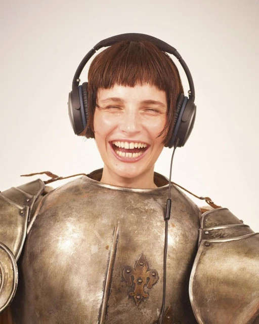 Smiling woman in medieval armor wearing headphones against a neutral background. Shot in a photo studio with medium framing and bright lighting.
