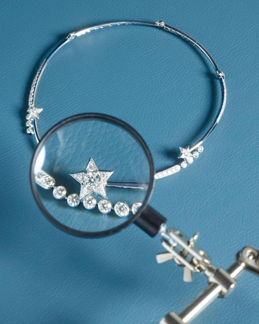Sparkling diamond star choker necklace on blue surface being examined with a small magnifying glass and articulated tool arm.