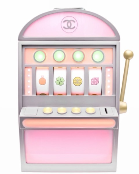 Slot machine with an off-white, silver and pink design featuring Chanel logo. Gambling themed toy is on a white background.