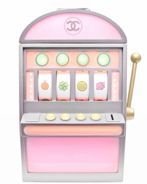 Slot machine with an off-white, silver and pink design featuring Chanel logo. Gambling themed toy is on a white background.
