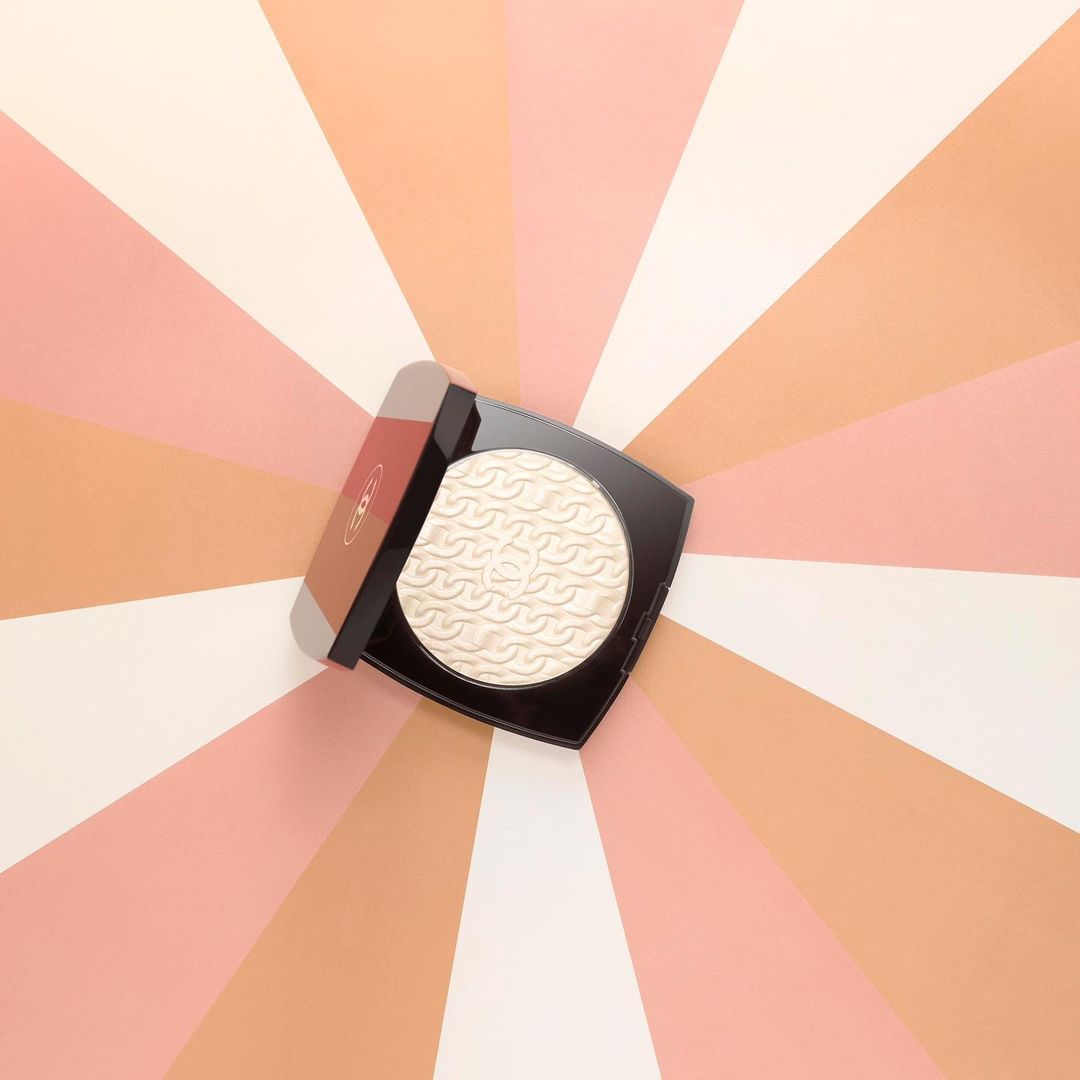 Overhead shot of Chanel powder compact with open lid against a colorful pink, peach, and white striped background.