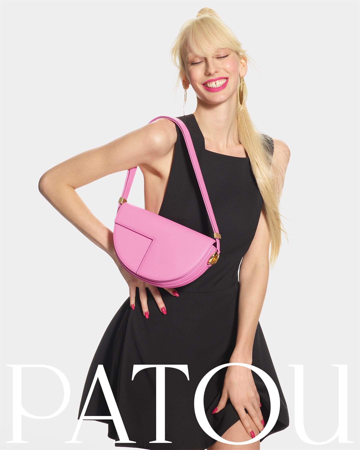 Fashionable woman wearing a black dress and a pink purse, posing in a studio with a white background. Beauty and style editorial.