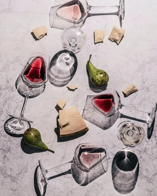 Overhead shot of red and white wine in glasses with pears and parmesan cheese on a textured light gray surface.