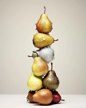 Stack of colorful pears covered in water droplets against a neutral background. Food photography showcasing freshness and variety.