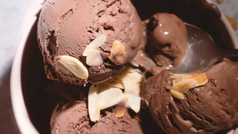 Bowl filled with scoops of rich chocolate ice cream, generously topped with sliced almonds, under a soft, diffused light.