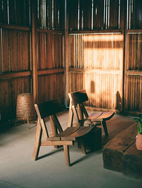 Interior of a room with two wooden chairs, a side table, and wooden slat walls, creating a minimalist and warm space.