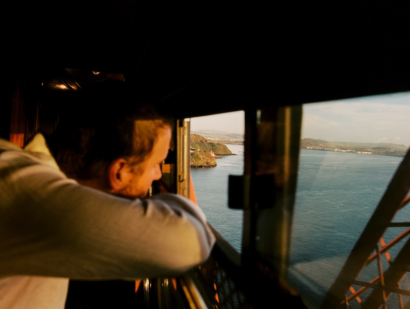 Adult male looks out over the Firth of Forth from the Forth Bridge, with land and water visible through the bridge's metal framework.