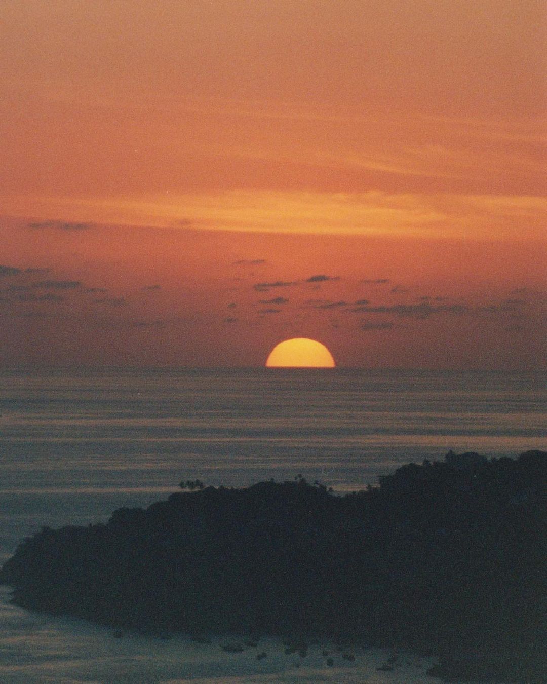 Orange sunset over a tranquil ocean landscape with a silhouetted island in the foreground, creating a serene and picturesque scene.