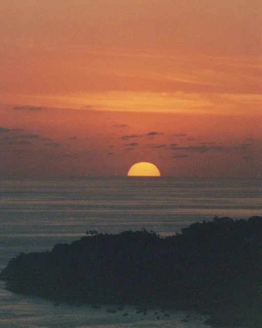 Orange sunset over a tranquil ocean landscape with a silhouetted island in the foreground, creating a serene and picturesque scene.