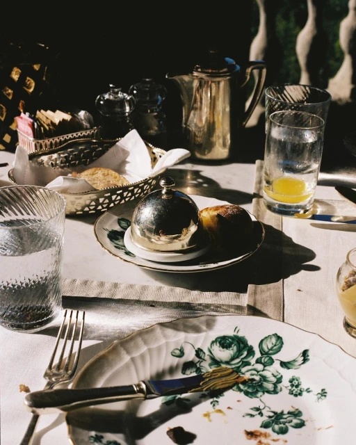Overhead shot of breakfast table setting featuring silverware, glassware, and china with floral patterns, bathed in natural light.