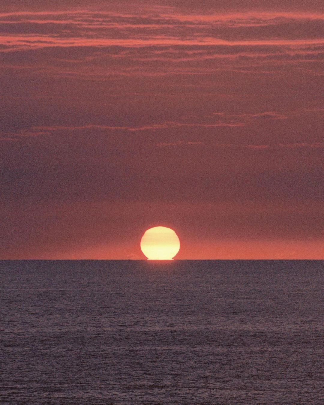 Vibrant sunset over the ocean, featuring a yellow sun near the horizon, creating a gradient sky with orange and red hues.