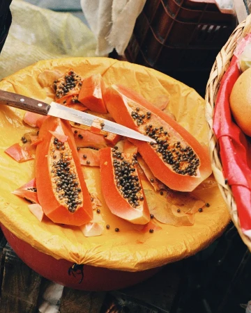 Overhead shot of sliced papaya on a yellow surface with a knife, displaying the orange flesh and black seeds of the fruit.