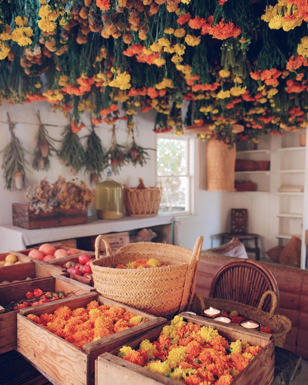 Indoor market scene with wooden boxes of orange and yellow flowers, baskets, and hanging dried flowers creating a warm, rustic aesthetic.