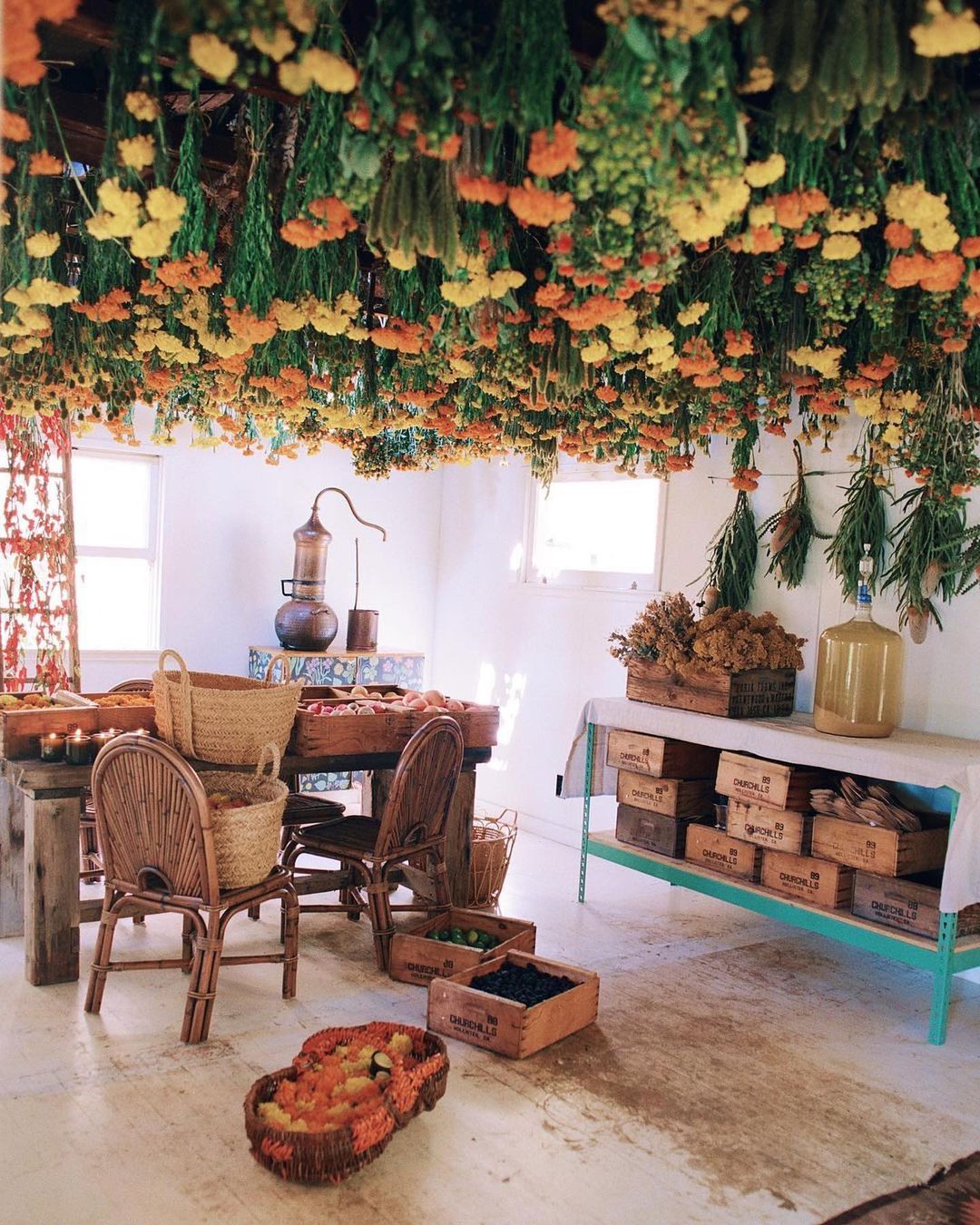 Indoor space filled with tables, chairs, and vintage decor, highlighted by dried flowers hanging from the ceiling, creating a rustic ambiance.