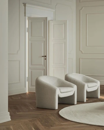 Interior photography of two white upholstered chairs and a round rug on a wood floor near a doorway in a room with white walls.