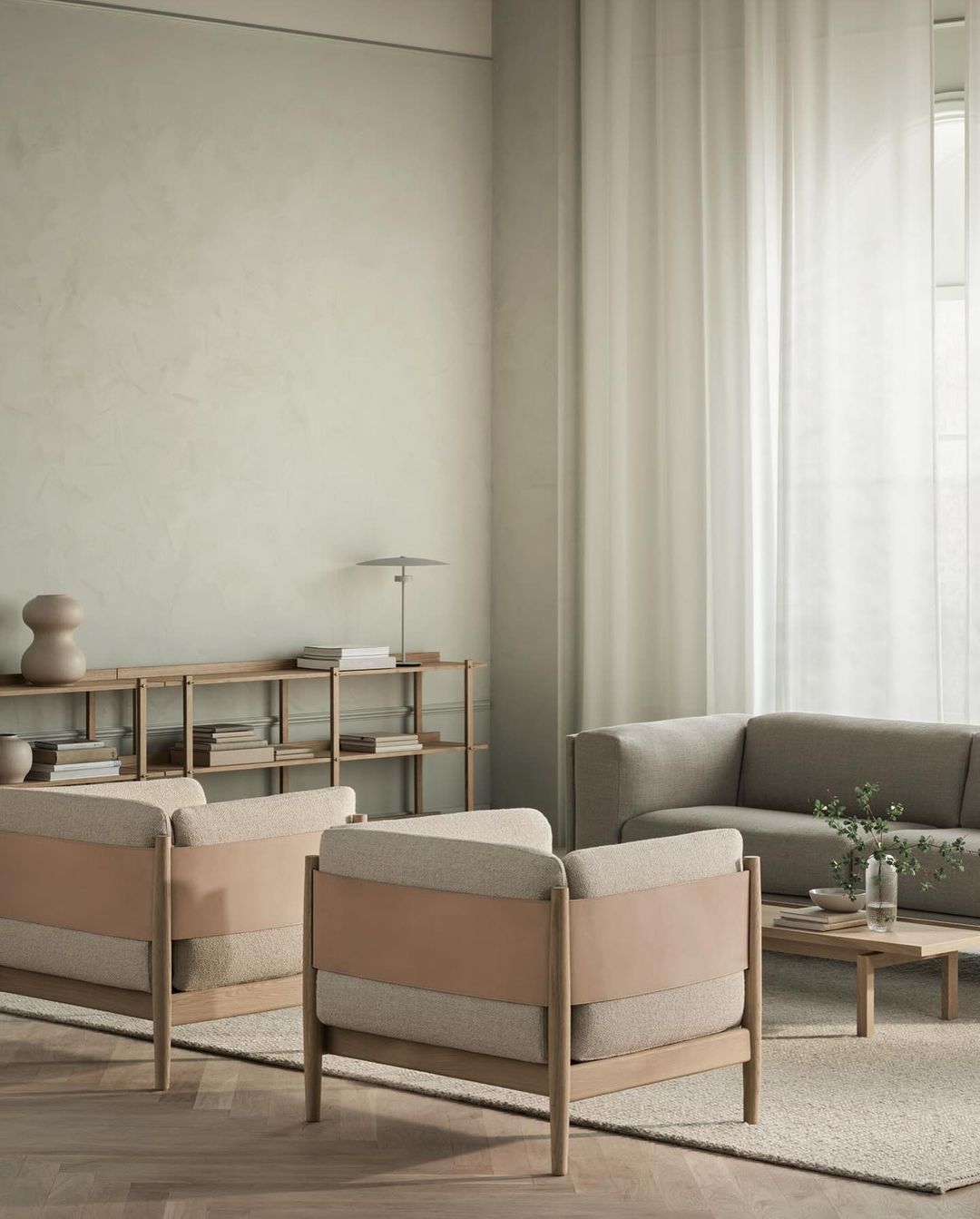 Living room interior featuring two armchairs with tan leather and light wood frames, soft neutral sofa, wood shelving, and pale green walls.