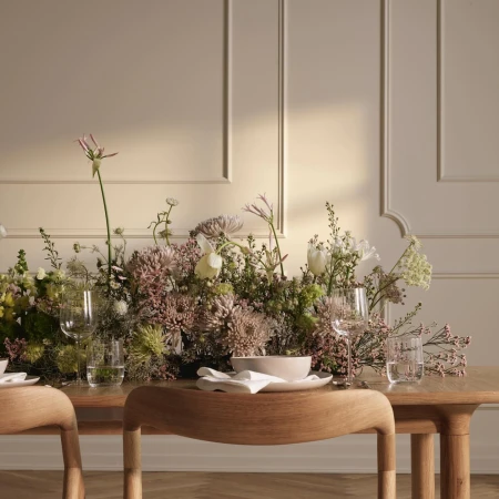 Elegant dining setup featuring a wooden table adorned with a lush floral arrangement, glassware, and plates against a neutral background.