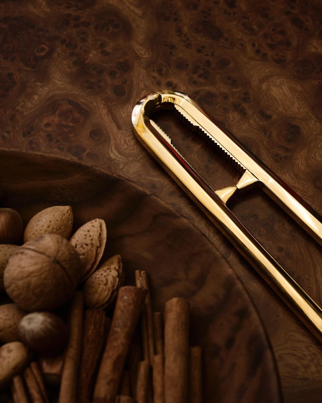 Close-up studio shot of golden nutcracker resting on a brown wooden bowl with almonds and cinnamon sticks, showcasing food photography.