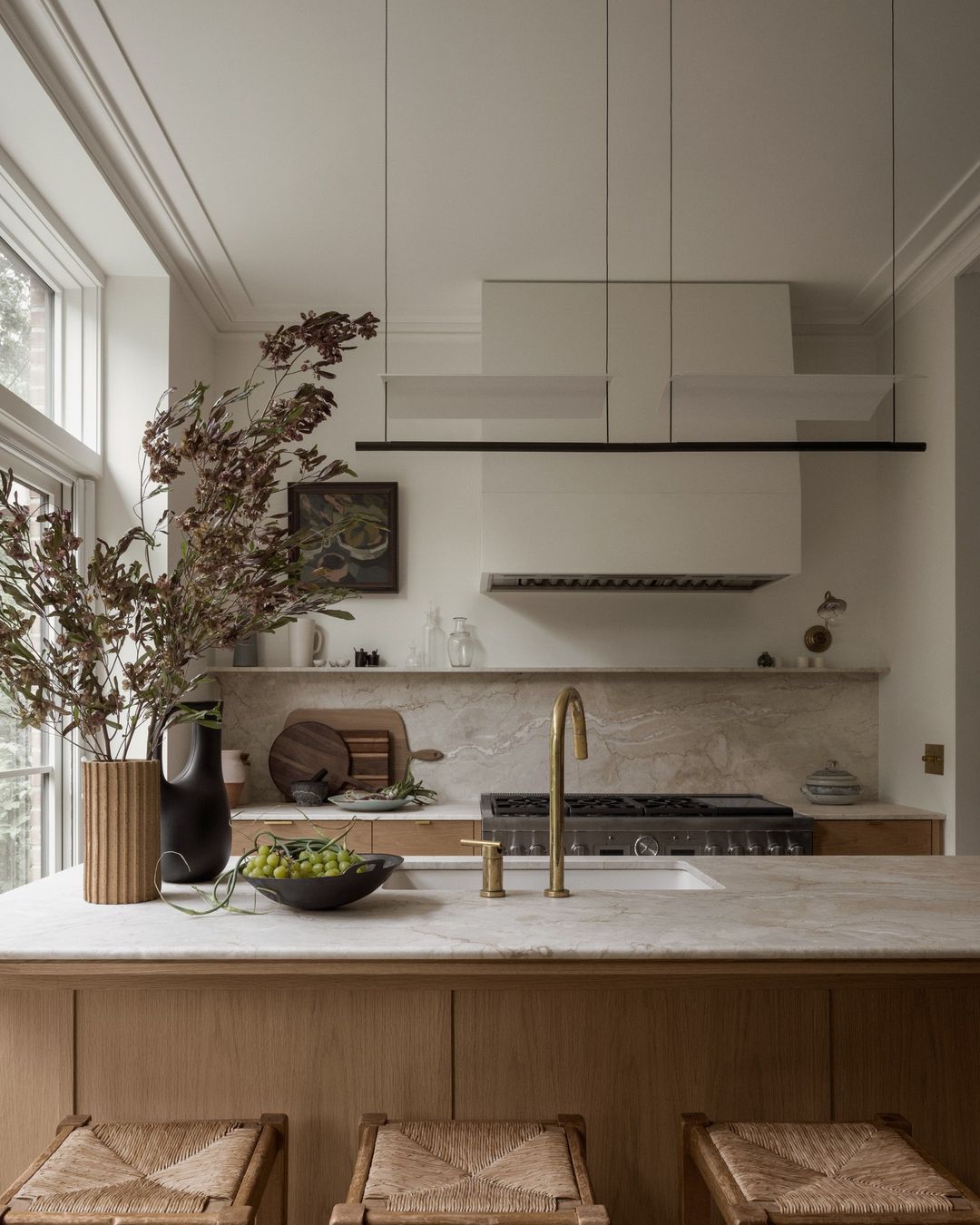 Stylish kitchen interior featuring a marble countertop island with woven stools, a gold faucet, and decorative dried foliage.