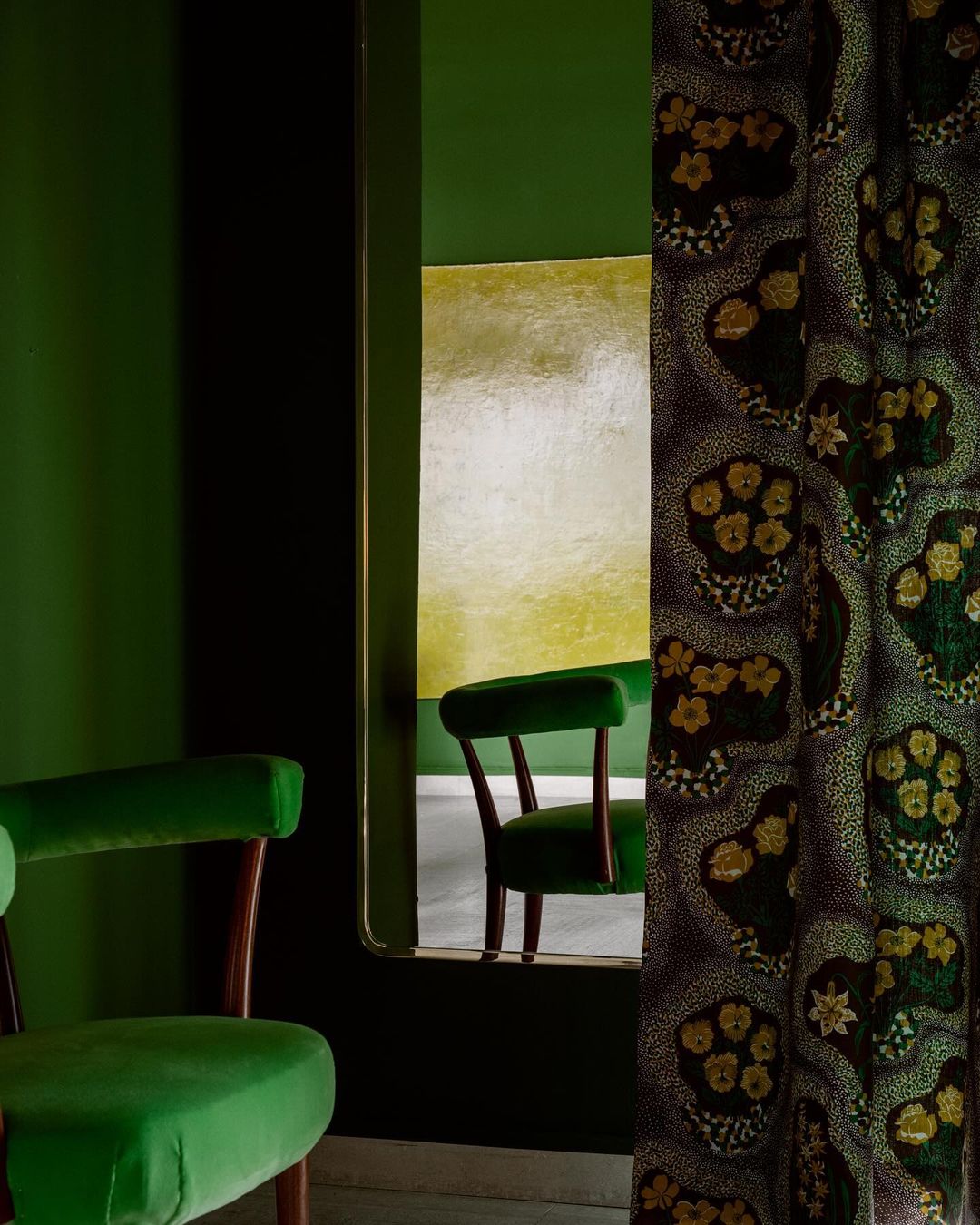 Interior view of green chair, ornate curtain, and reflection of chair in mirror against a green and yellow background indoors.