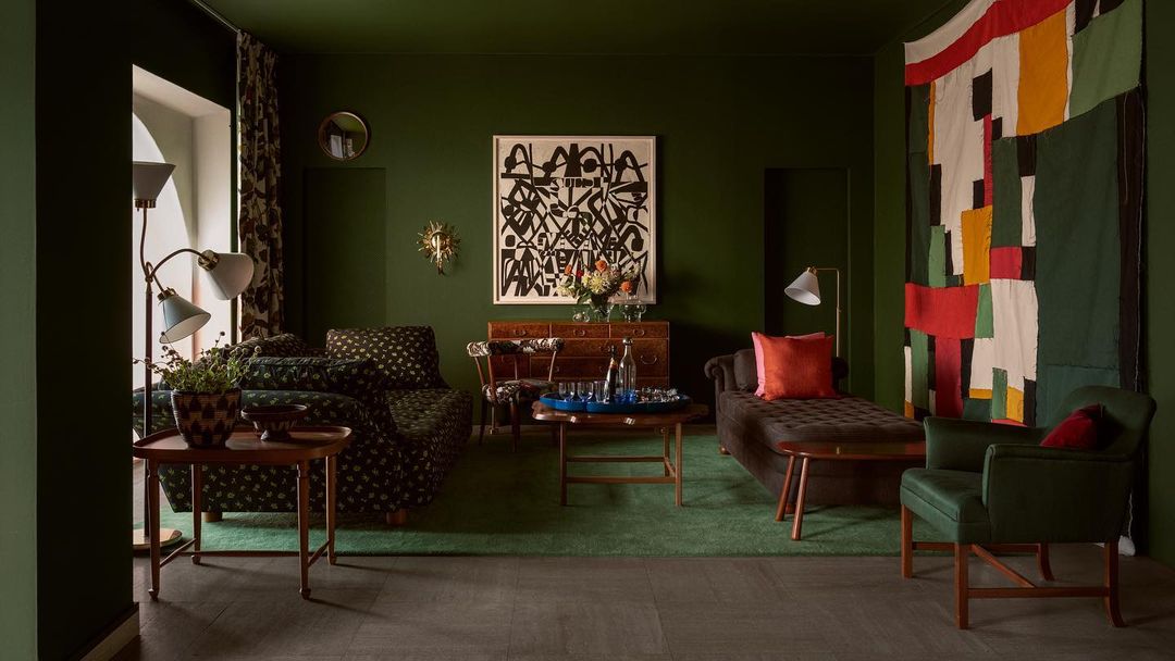 Living room interior with floral patterned sofa, chaise lounge, colorful textile wall art, and green walls creating a coordinated aesthetic.