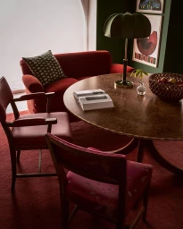 Interior dining space featuring a round wooden table, red upholstered armchairs, and a matching red sofa in Los Angeles by Pia Ulin.