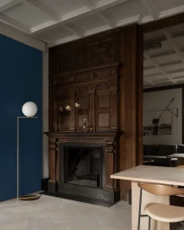 Interior shot of an ornate dark wood fireplace mantel, blue accent wall, and a modern globe floor lamp by photographer Pia Ulin.