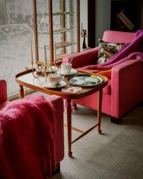 Interior setting with pink armchairs, wooden coffee table, tea set, playing cards, and a glass display cabinet by Pia Ulin