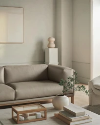 Minimalist living room interior featuring a beige leather sofa and a coffee table with stacked books and a vase.